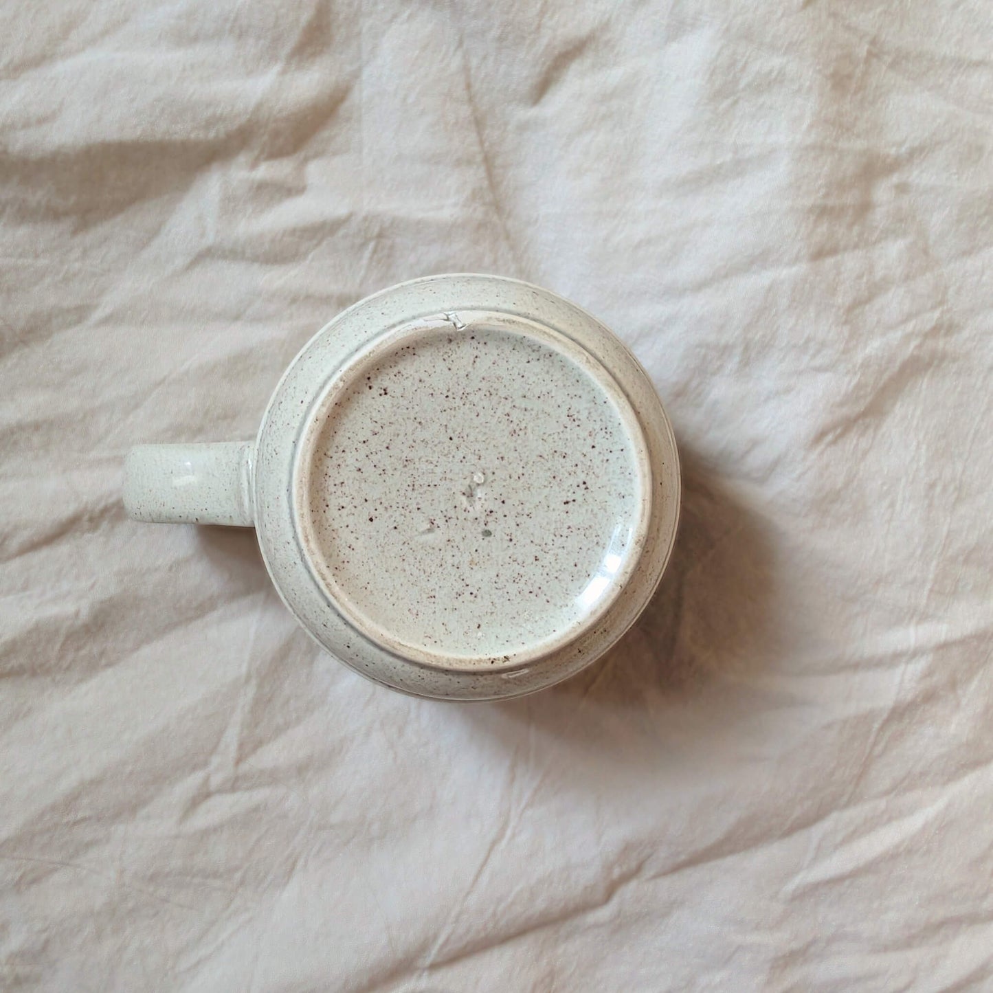 The bottom of a vintage, ceramic teacup. Cream glaze with brown specks.