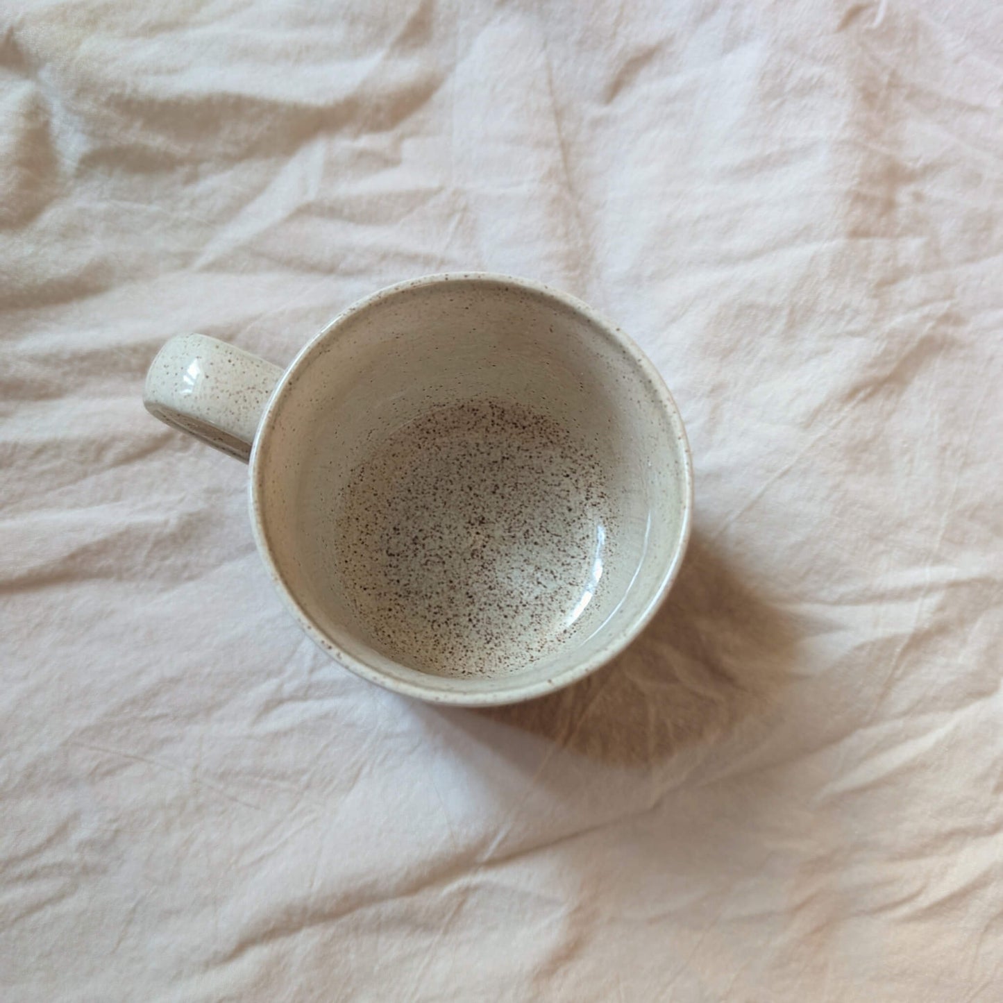 The top of a vintage, ceramic teacup. Cream glaze with brown specks. No chips or cracks.