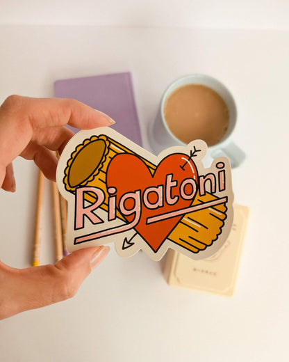 Hand holding a 'Rigatoni' sticker with heart design on a light background