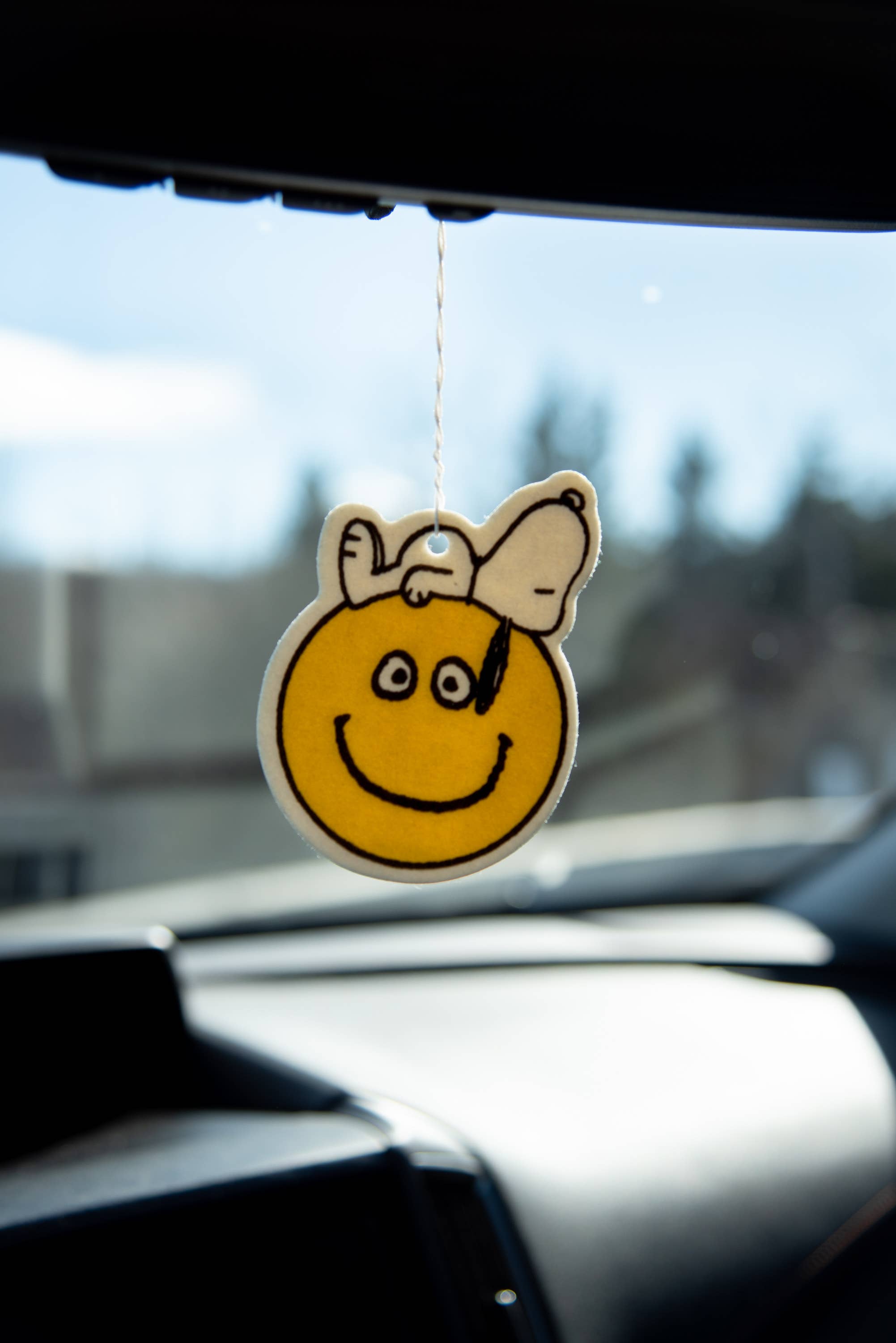 Snoopy car air freshener with smiley design hanging from car window