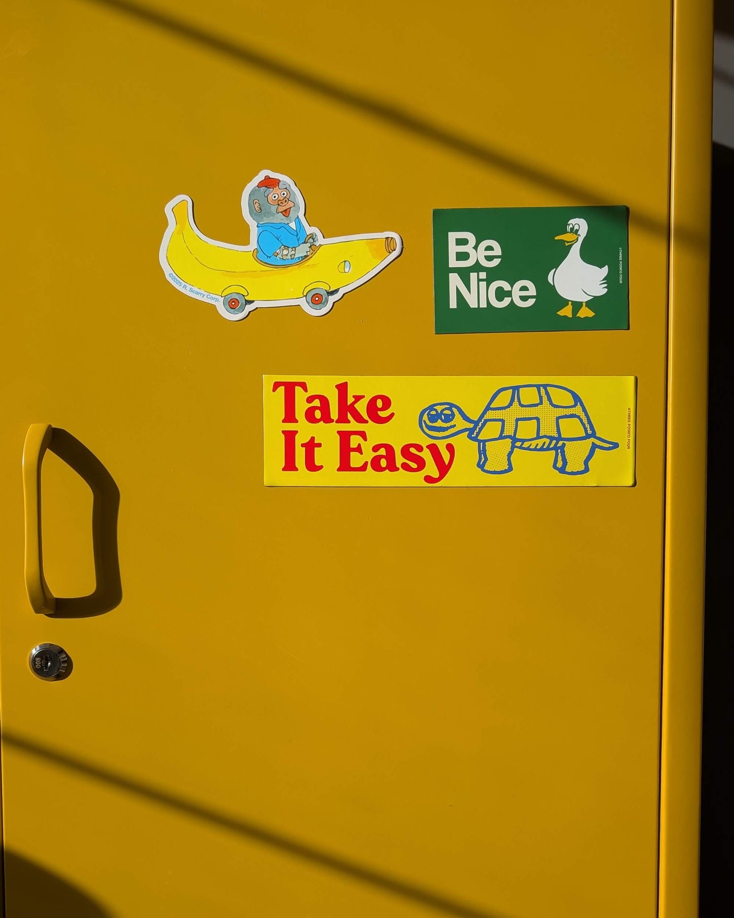 Yellow door with stickers including a turtle, banana character, and duck with 'Be Nice' text.