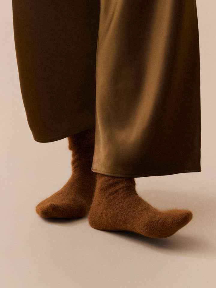 Brown socks worn with a long brown coat on a plain background