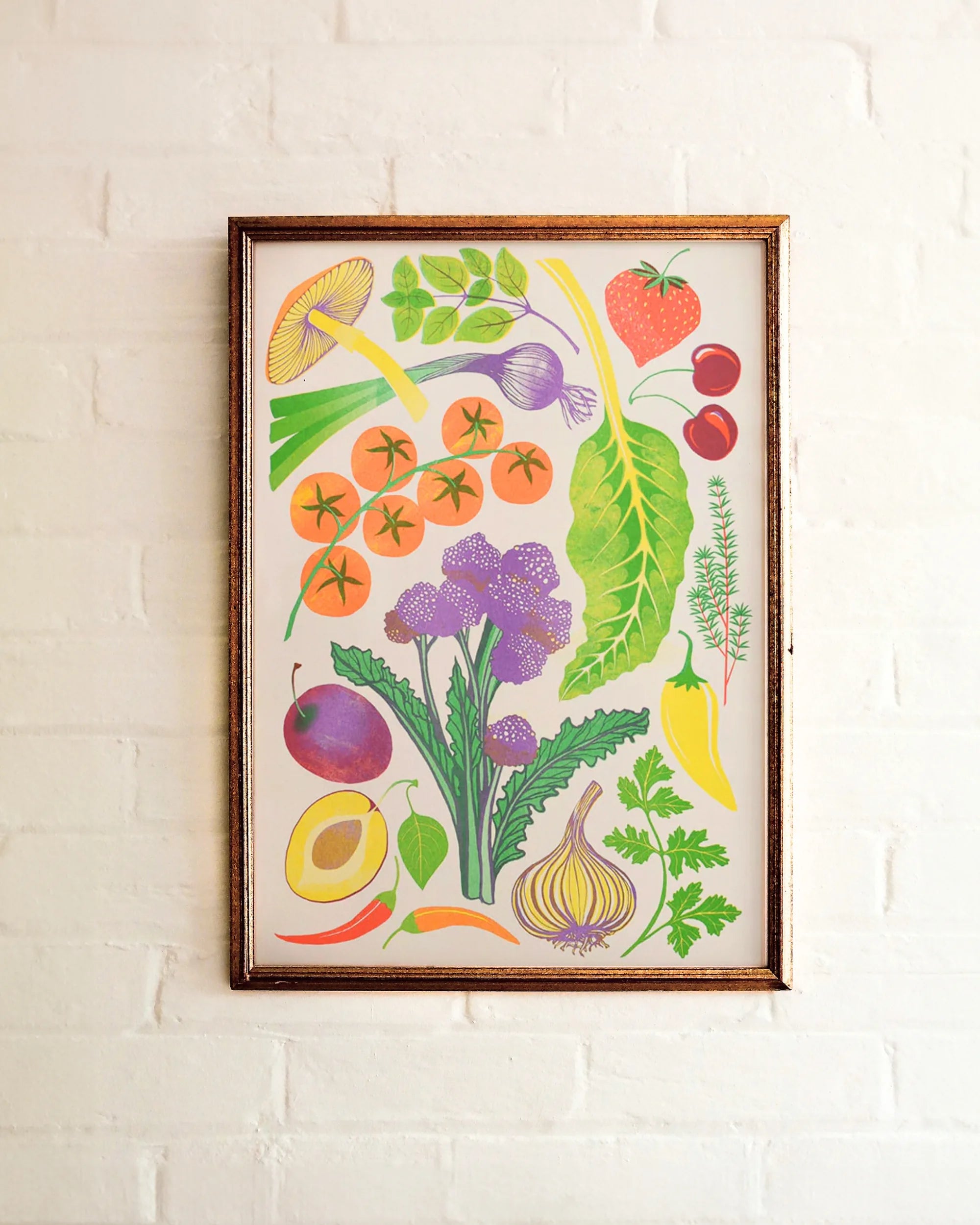 Framed riso print of colourful fruits and vegetables on a white brick wall.