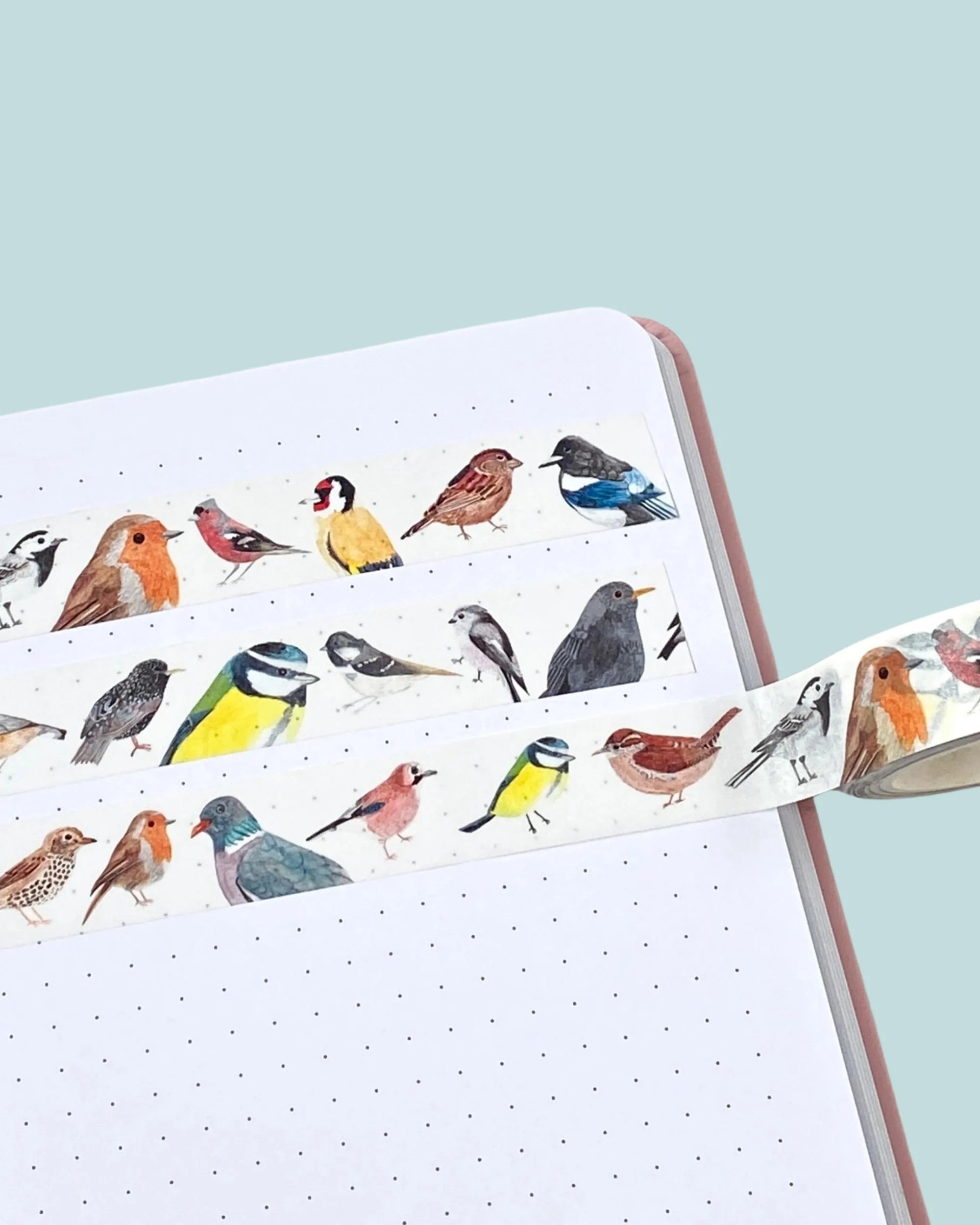 Roll of decorative washi tape with bird designs on a notebook with a light blue background
