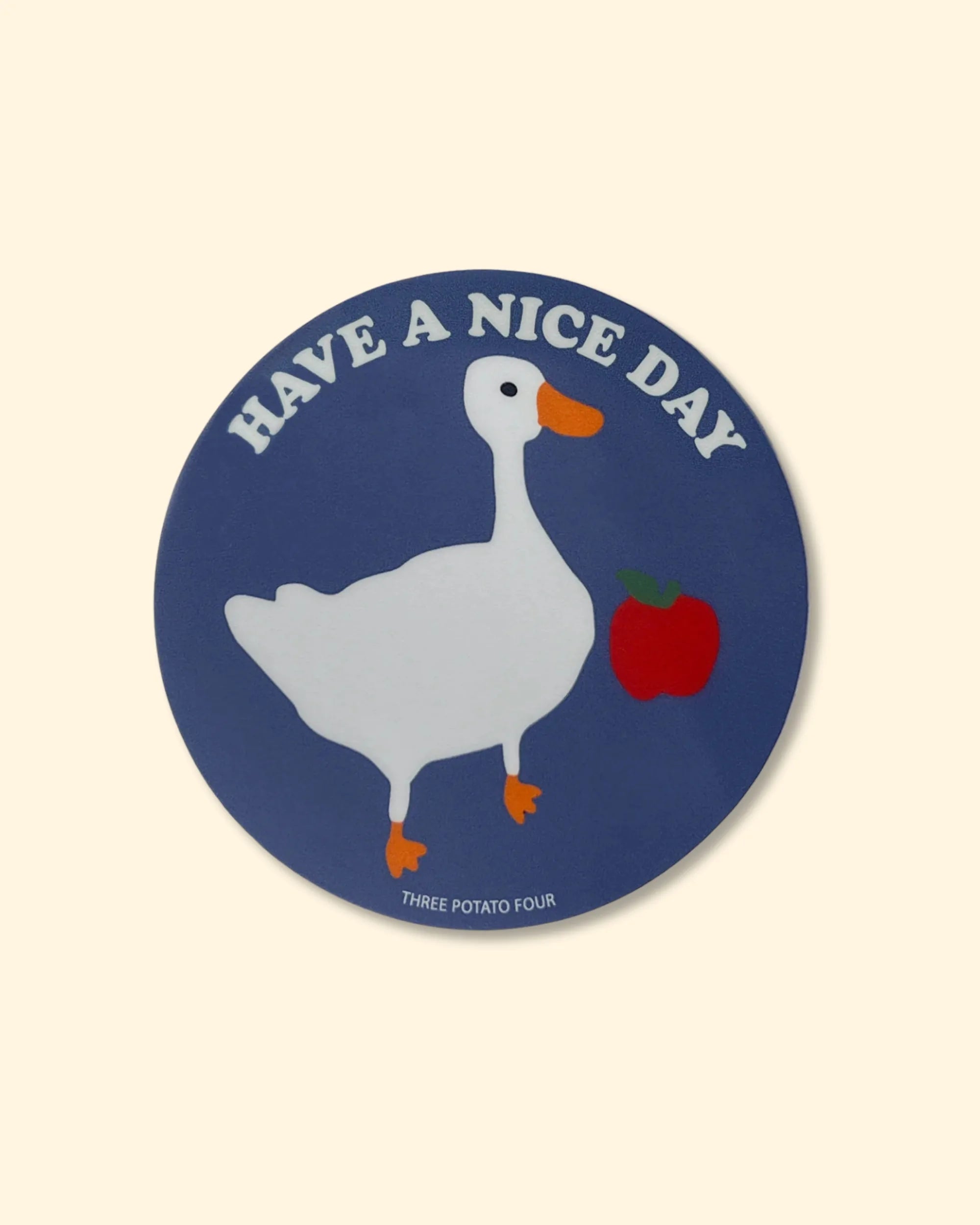 Round blue sticker with a duck and apple illustration and 'Have a nice day' text on a beige background.