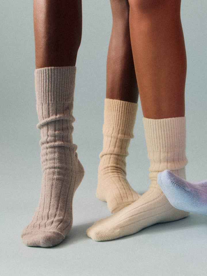 Two pairs of feet wearing beige socks on a neutral background