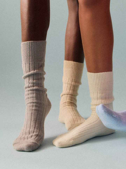 Two pairs of feet wearing beige socks on a neutral background