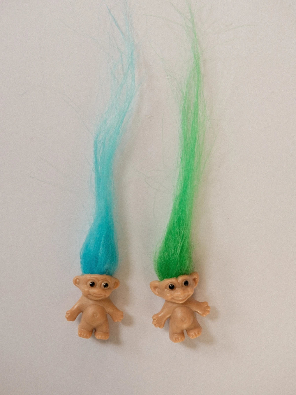 Flat lay of two mini troll dolls with blue and green hair on white background