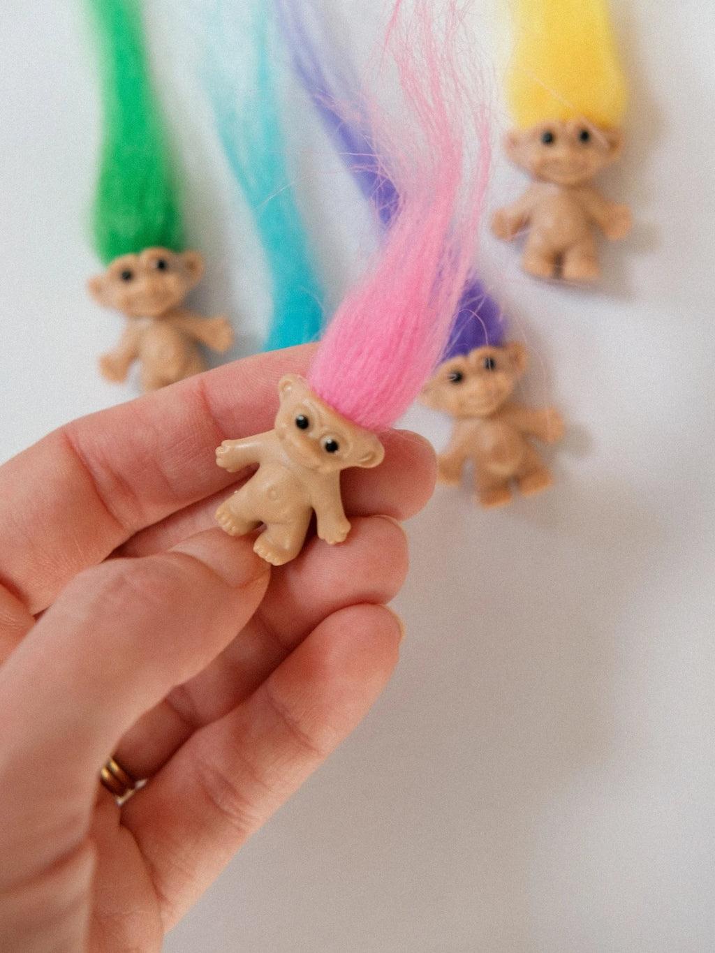 Hand holding a miniature pink hair troll doll with other coloured trolls behind