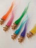 Seven miniature troll dolls with rainbow coloured hair laid out on white background

