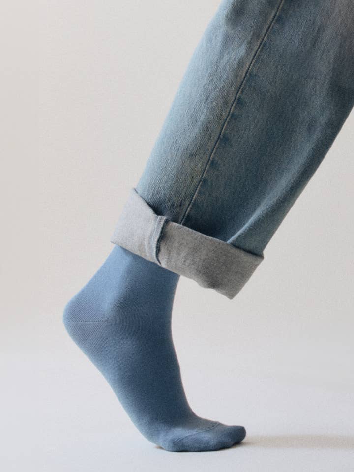 Person wearing light blue socks and rolled-up jeans on a plain background