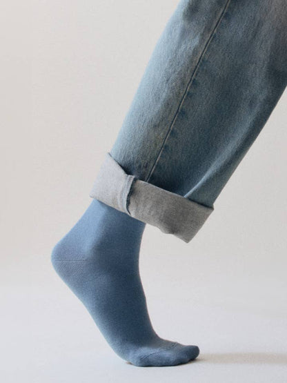Person wearing light blue socks and rolled-up jeans on a plain background