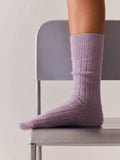 Person wearing purple socks sitting on a chair with a neutral background