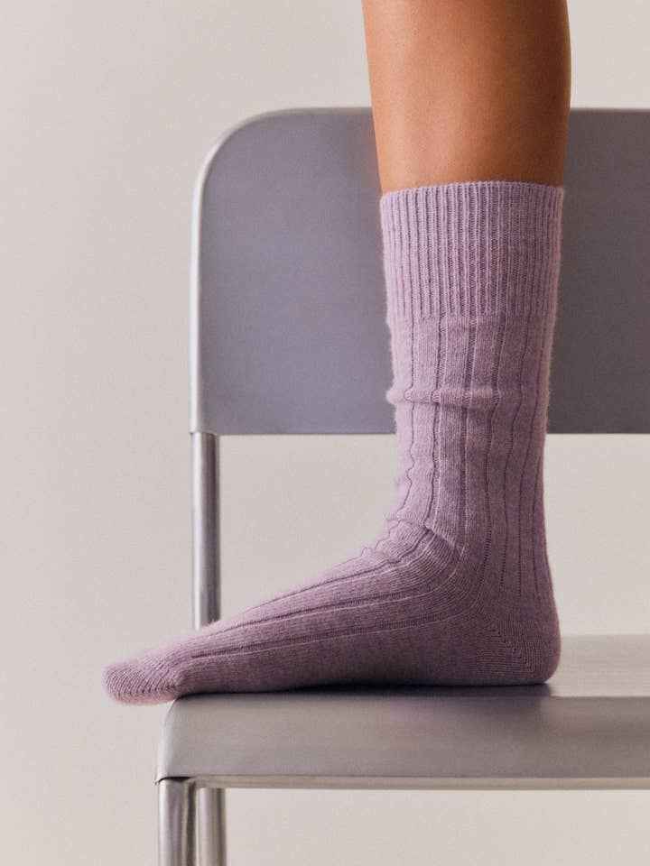 Person wearing purple socks sitting on a chair with a neutral background