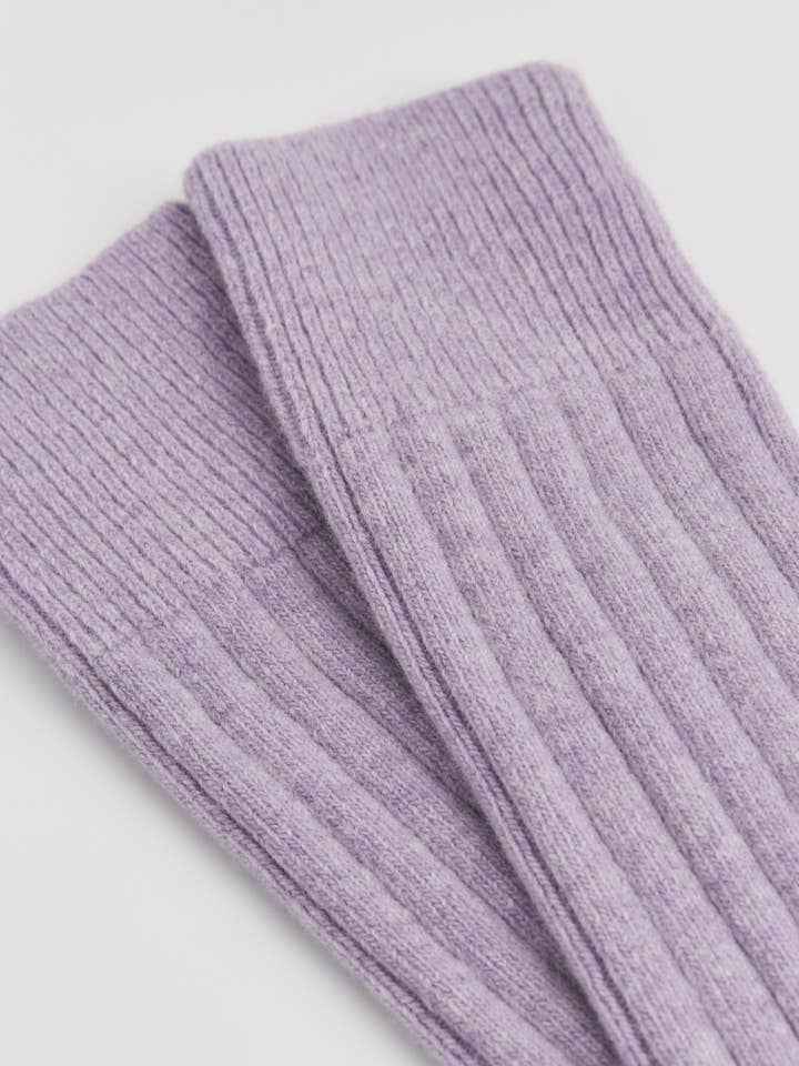 Purple ribbed knit merino bed socks on a light gray background