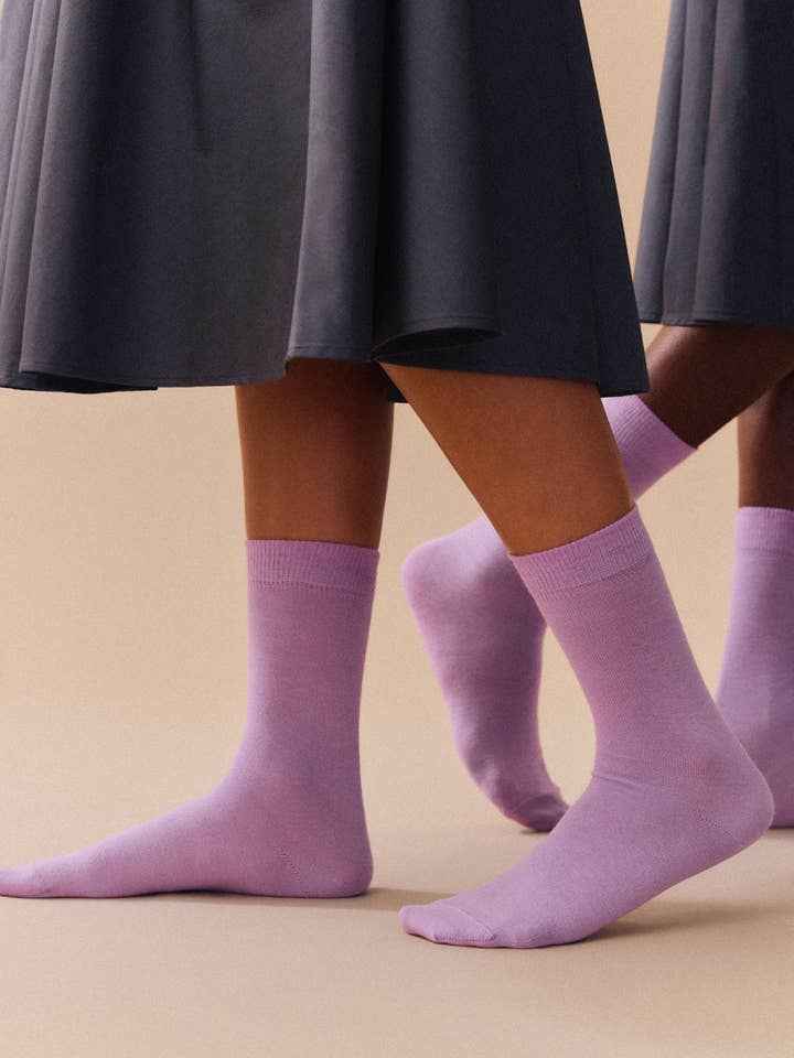 Purple socks worn with a dark skirt on a beige background