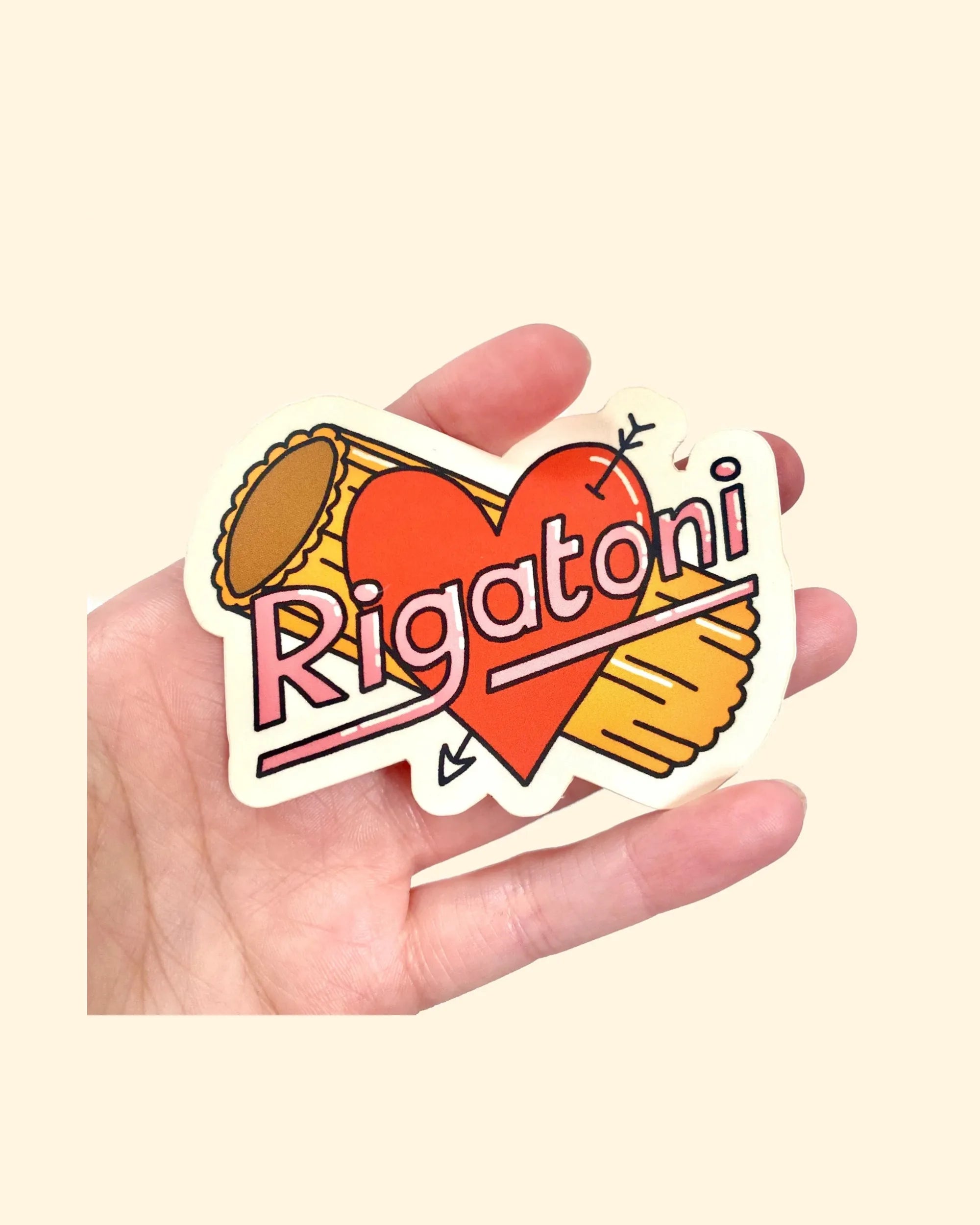 Hand holding a sticker with 'Rigatoni' text and heart design on a beige background