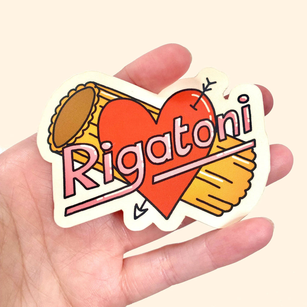 Sticker with heart and rigatoni pasta held in a hand against a beige background