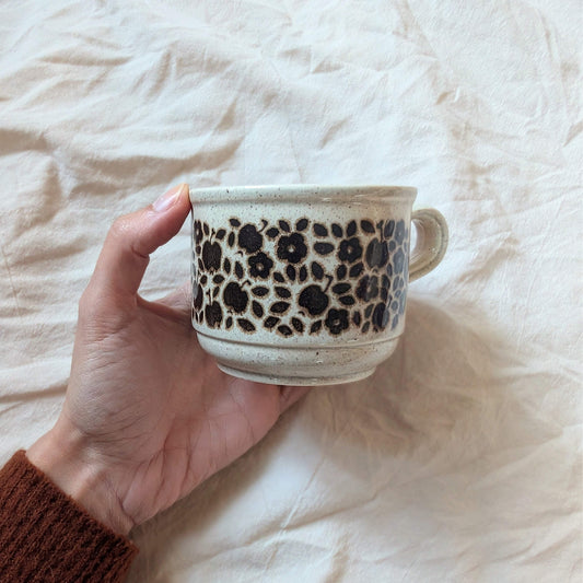 Hand holding a ceramic mug with floral patterns on a soft, light-colored fabric background